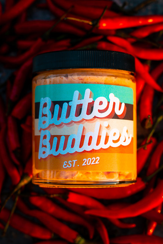 Flavoured Butter jar, Labeled "Butter Buddies" on top of a bed of spicy red chili peppers. 