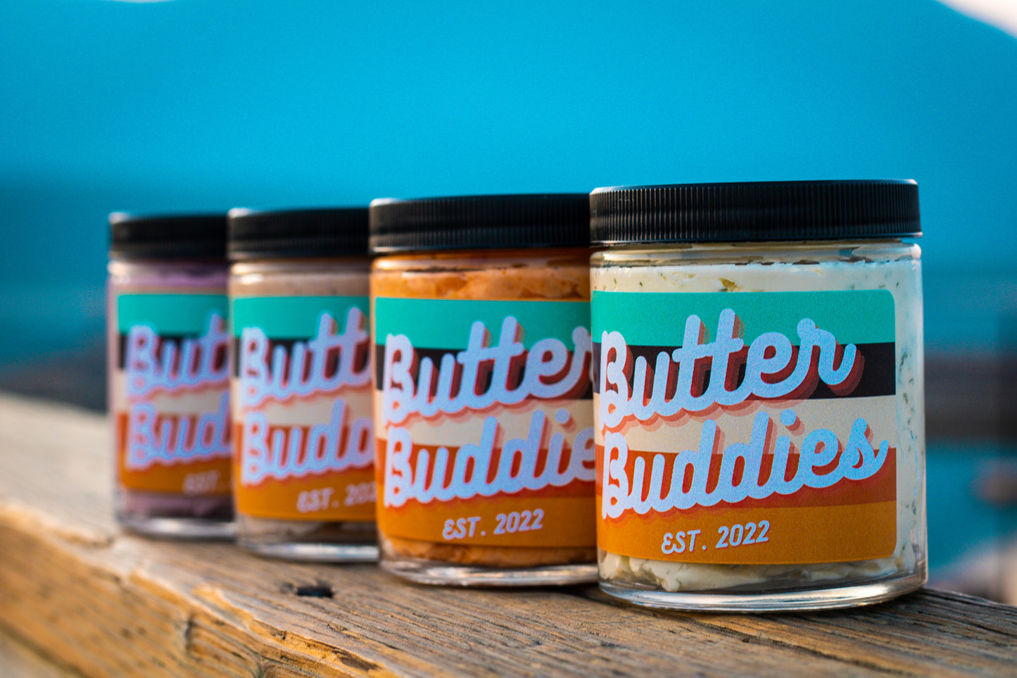 4 Flavours of Butter Buddies, lined up outdoors on a dock, with labels, showing the butter inside.