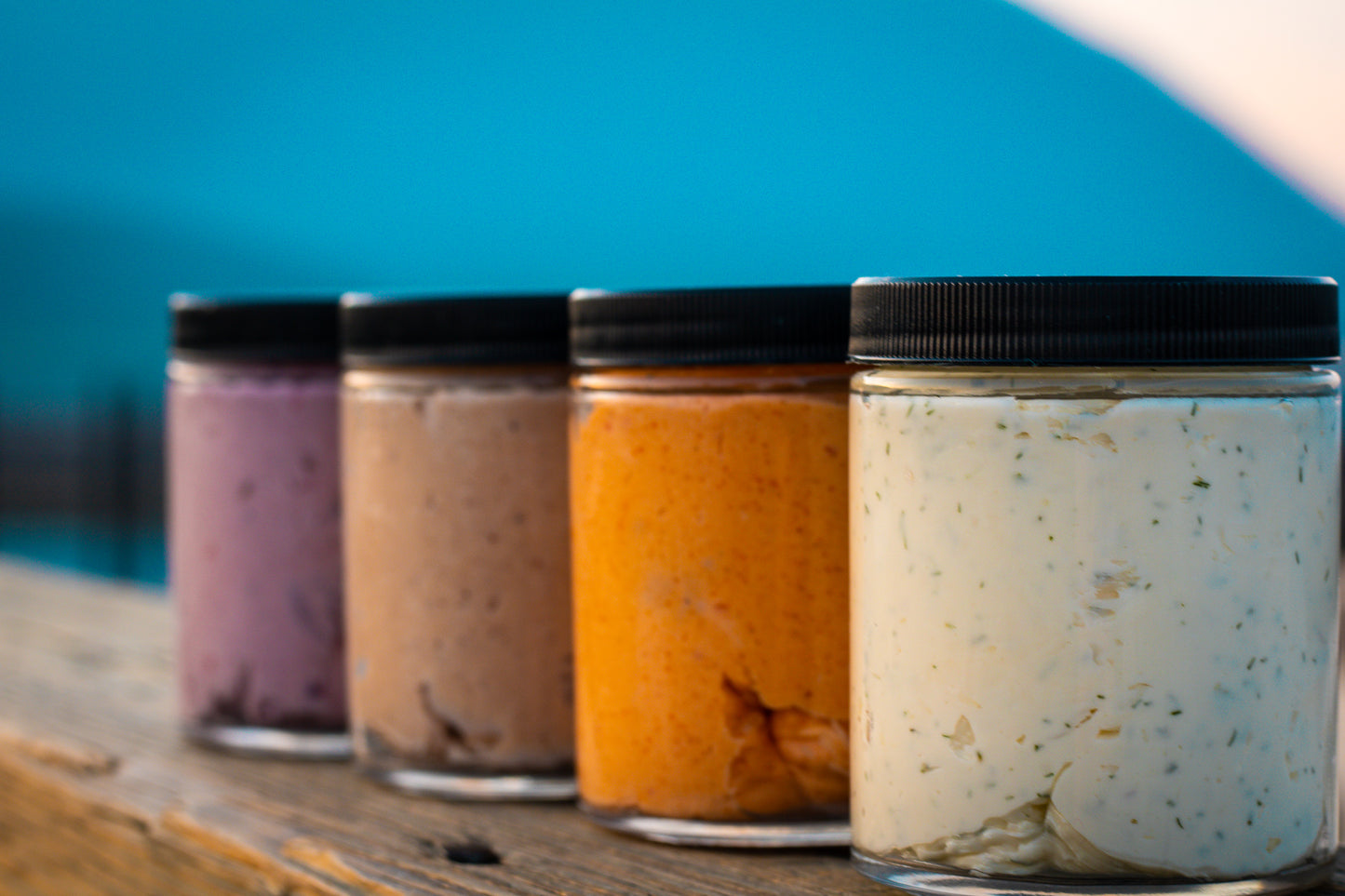 4 Flavours of Butter Buddies, lined up outdoors on a dock, without labels, showing the butter inside.
