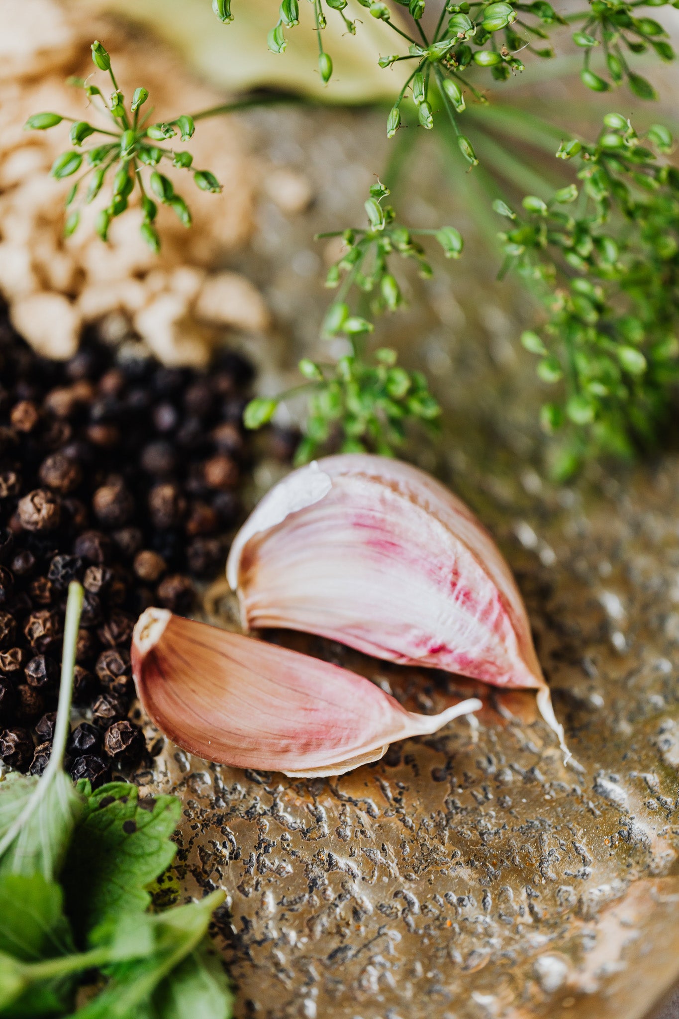 Closeup of garlic, dill, herbs and peppercorns on a cutting board.