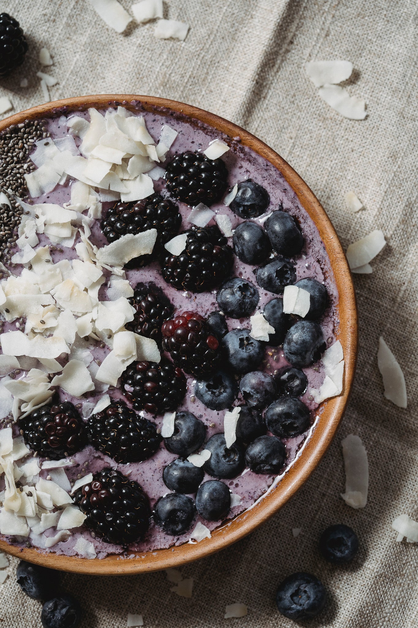 Oatmeal smoothie bowl with blueberrys, blackberrys, coconut and chia seeds in a wooden bowl.