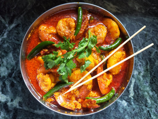 Hot thai shrimp in a bowl with chilis fresh herbs in a buttery sauce thats sweet with a little heat